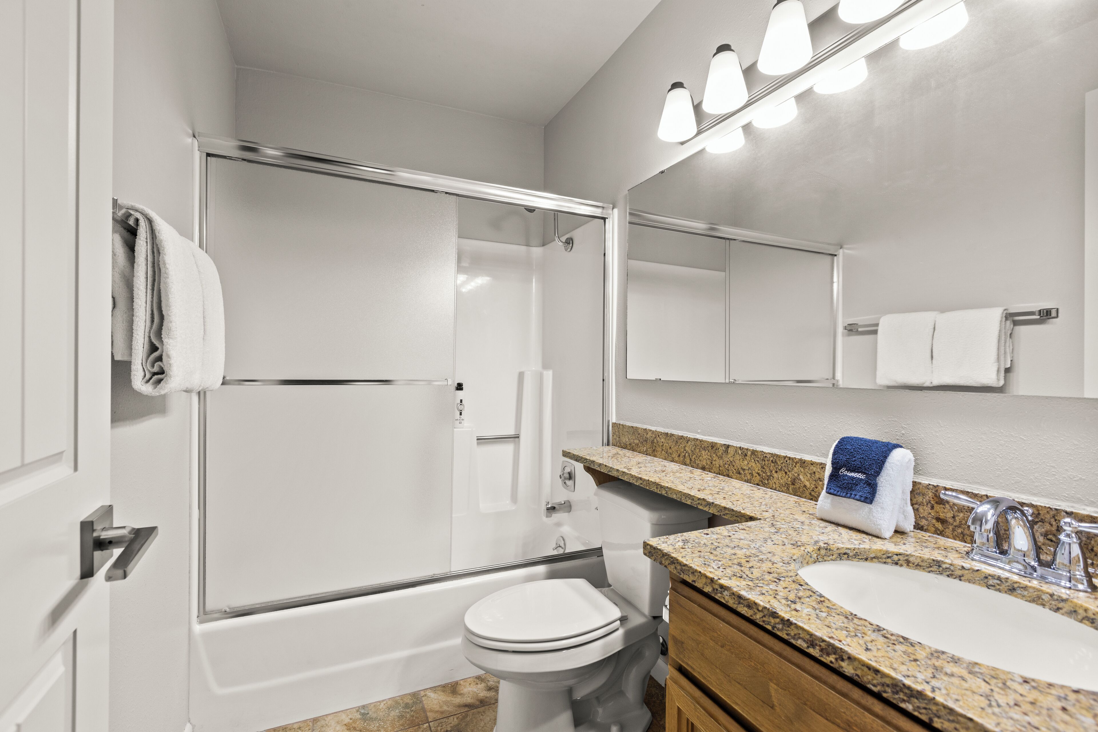 A modern bathroom with a glass-enclosed shower, a white toilet, a granite countertop sink, and a mirror above the sink.