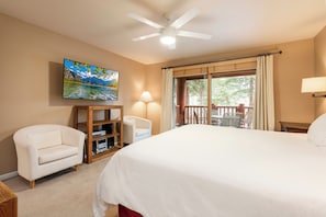 A hotel room with a large bed, a television mounted on the wall, a desk with a lamp, and a view of the outdoors through the window.
