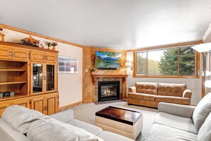 A living room with a fireplace, a television mounted on the wall, and a large window.