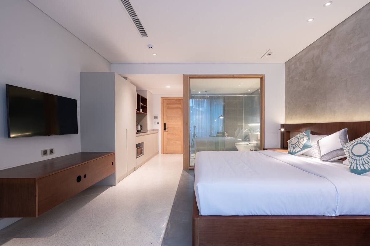 Een moderne hotelkamer met een groot bed, een televisie, een houten console en een douchecabine van glas.