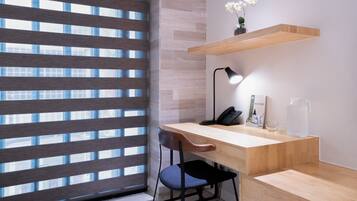 A modern office space with a wooden desk, a chair, a lamp, a phone, a vase with flowers, and a water pitcher.