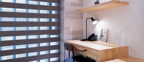A modern office space with a wooden desk, a chair, a lamp, a phone, a vase with flowers, and a water pitcher.