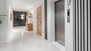 Een moderne hal met een houten deur, een glazen deur naar een balkon en een in de muur ingebouwde lift.