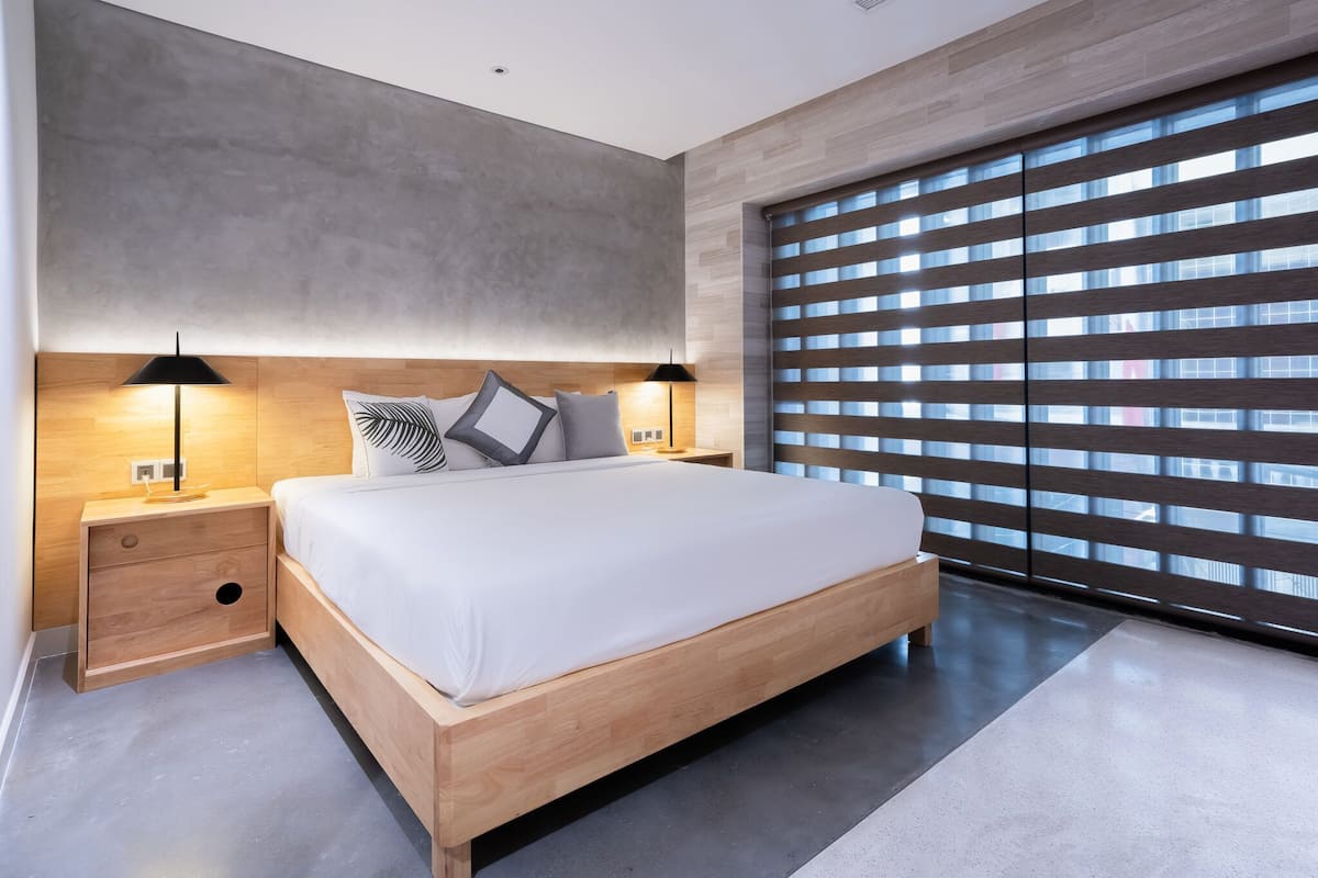 Een moderne slaapkamer met een groot bed, een houten hoofdbord, nachtlampjes en een uitzicht door het plafondhoge raam.