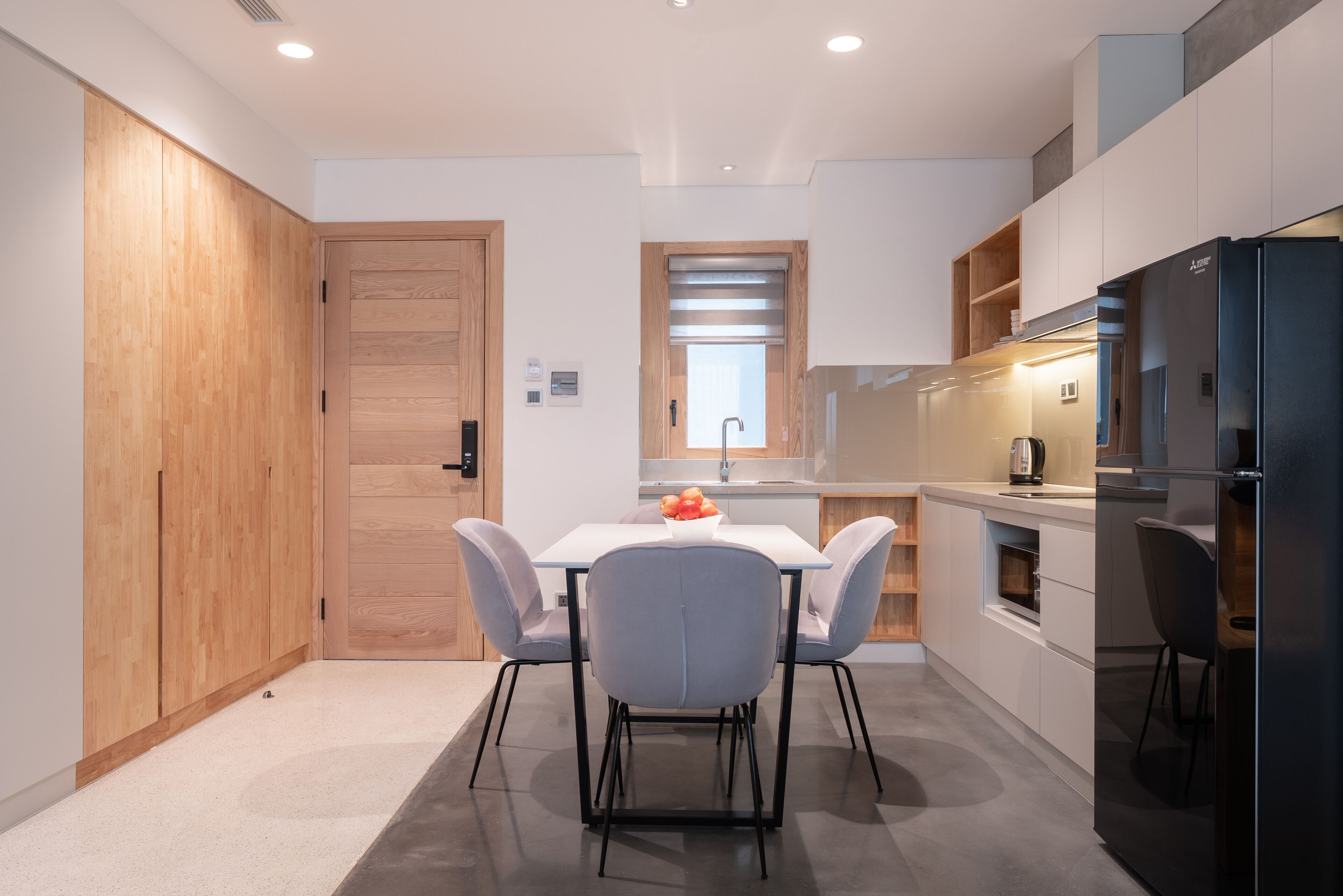 A modern kitchen with a wooden door, a white table with four chairs, and a black refrigerator.