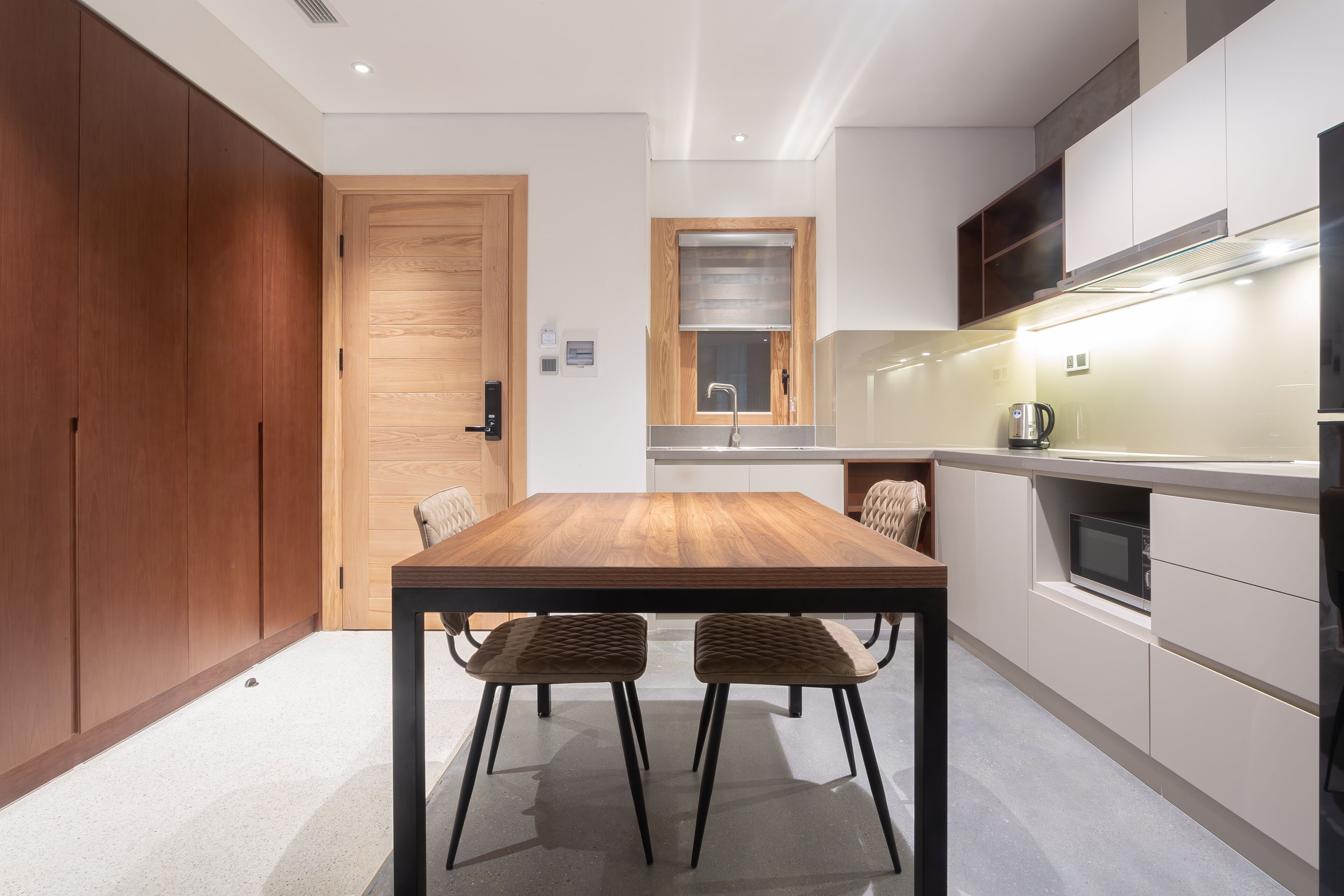 A modern kitchen with a wooden dining table, two cushioned chairs, and built-in appliances.