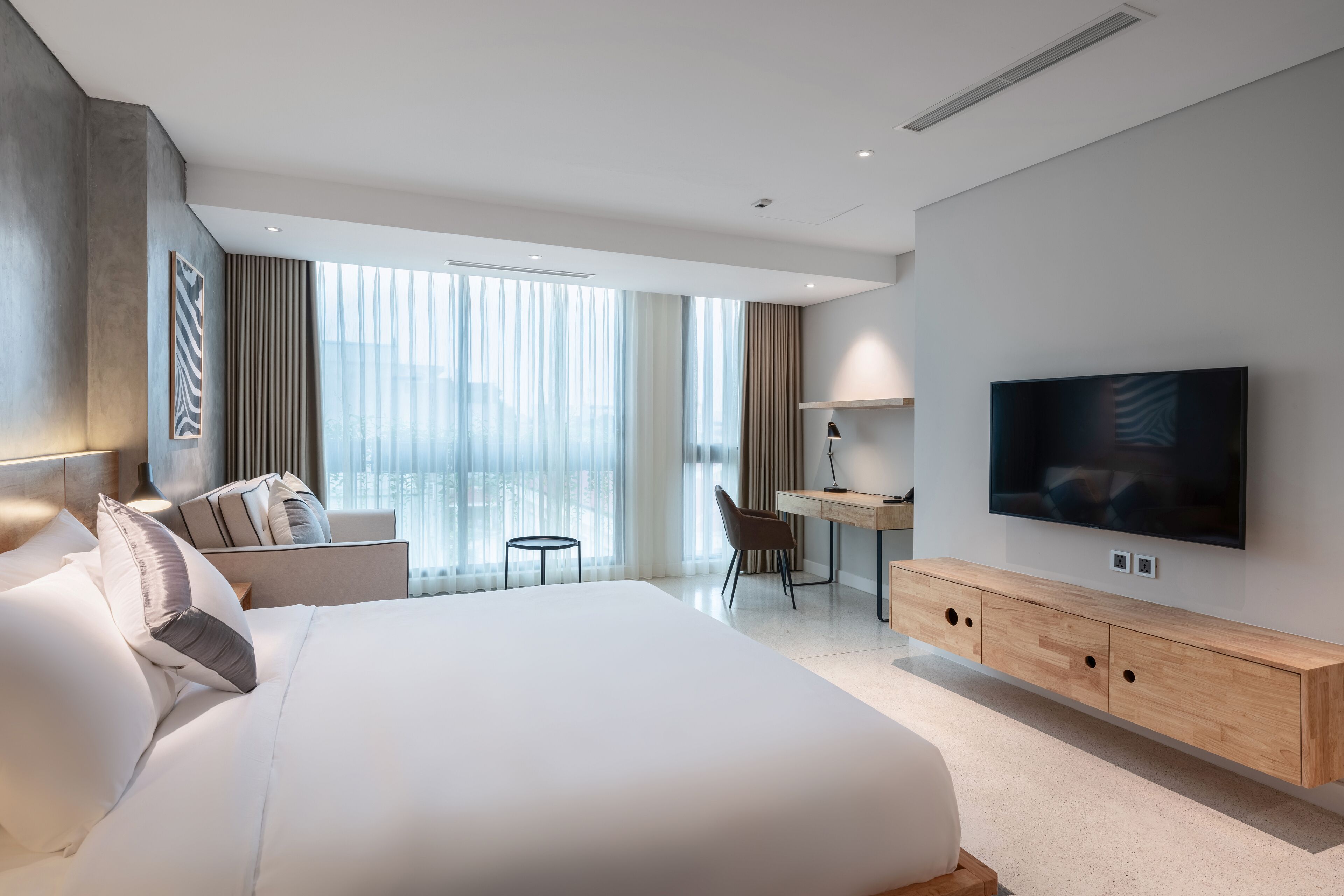 Habitación de hotel moderna con una cama grande, un escritorio, un televisor y vistas de la ciudad a través de amplias ventanas.