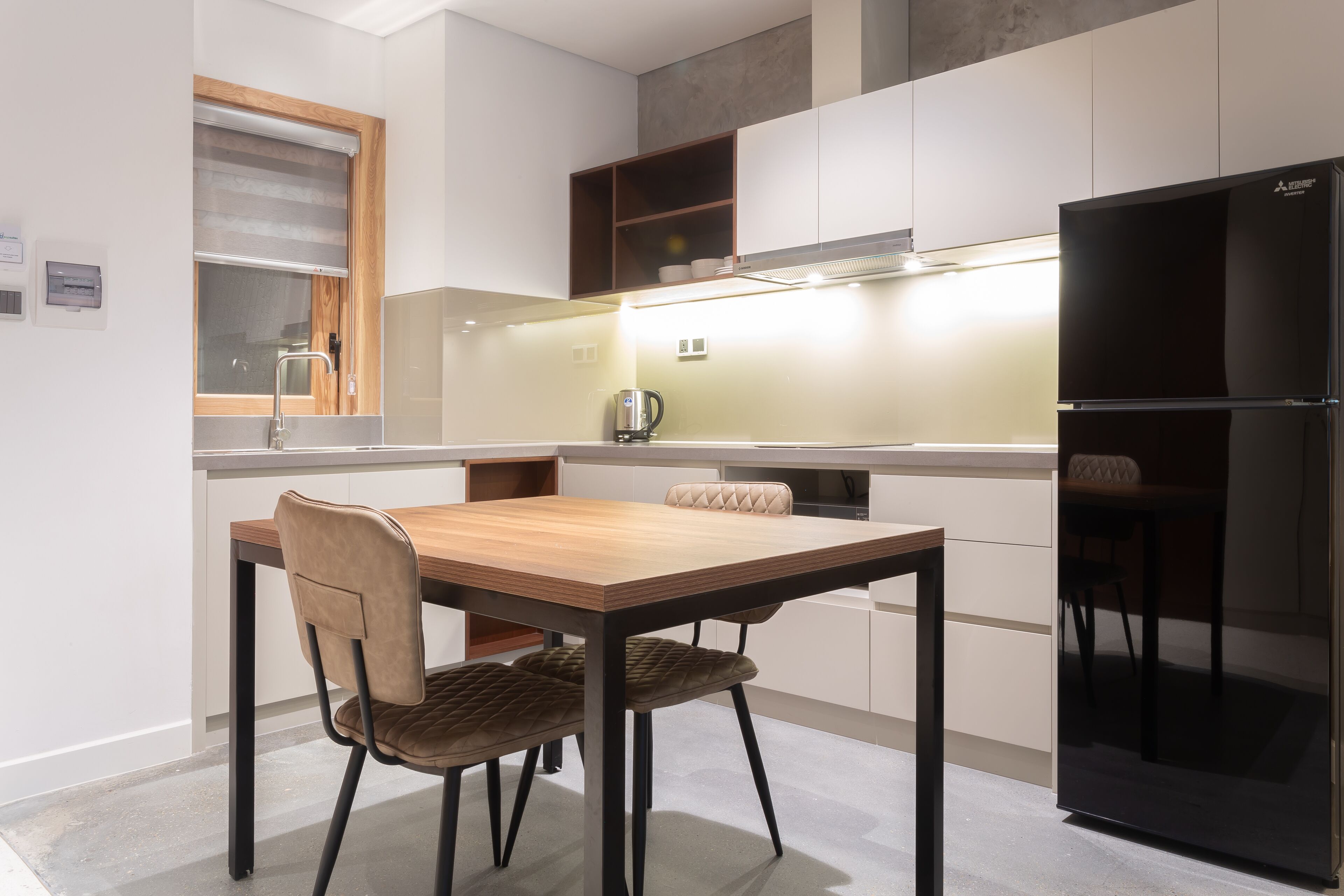 A modern kitchen with a wooden dining table, two chairs, a black refrigerator, and built-in cabinets.