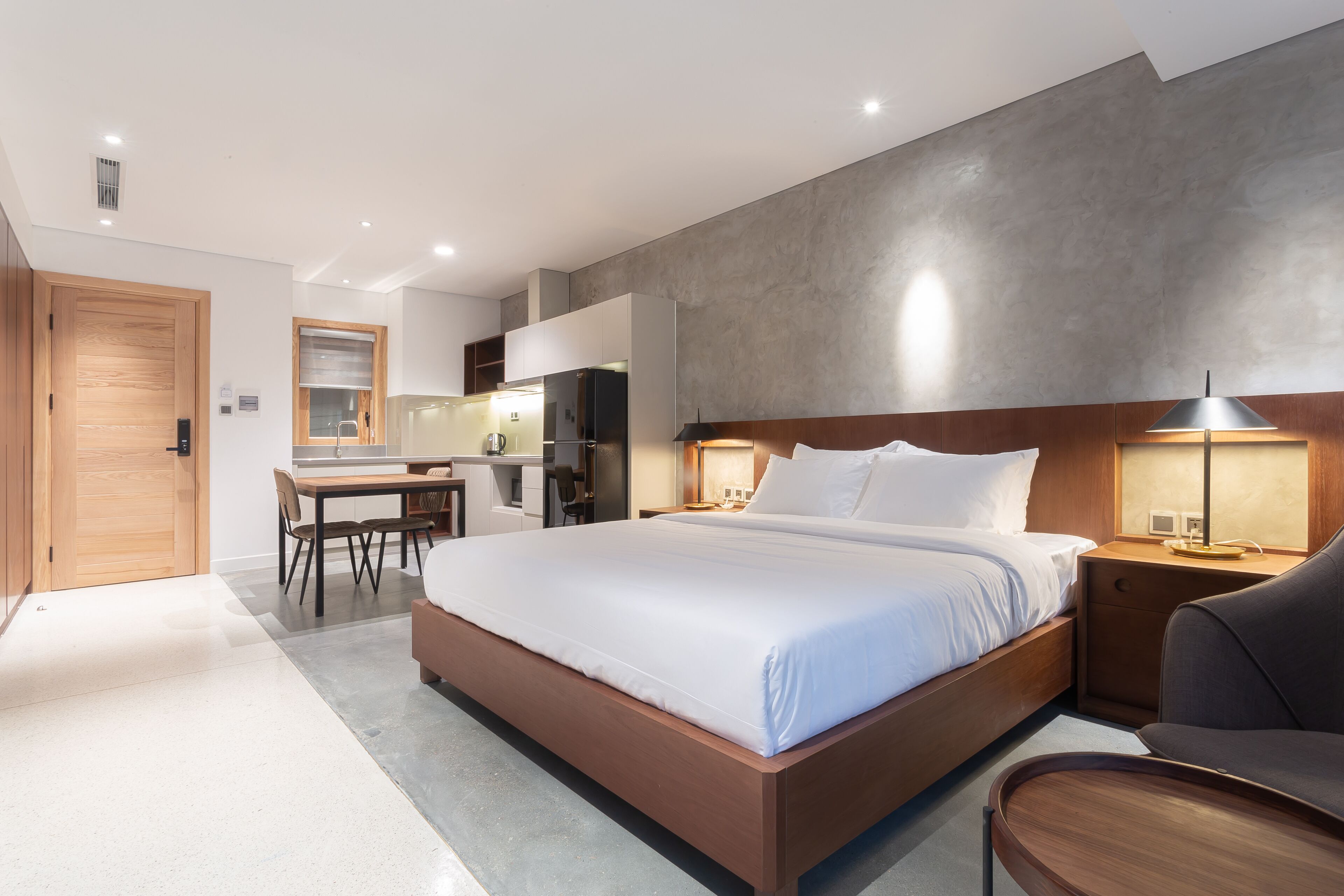 A modern hotel room with a large bed, a desk, and a kitchenette.