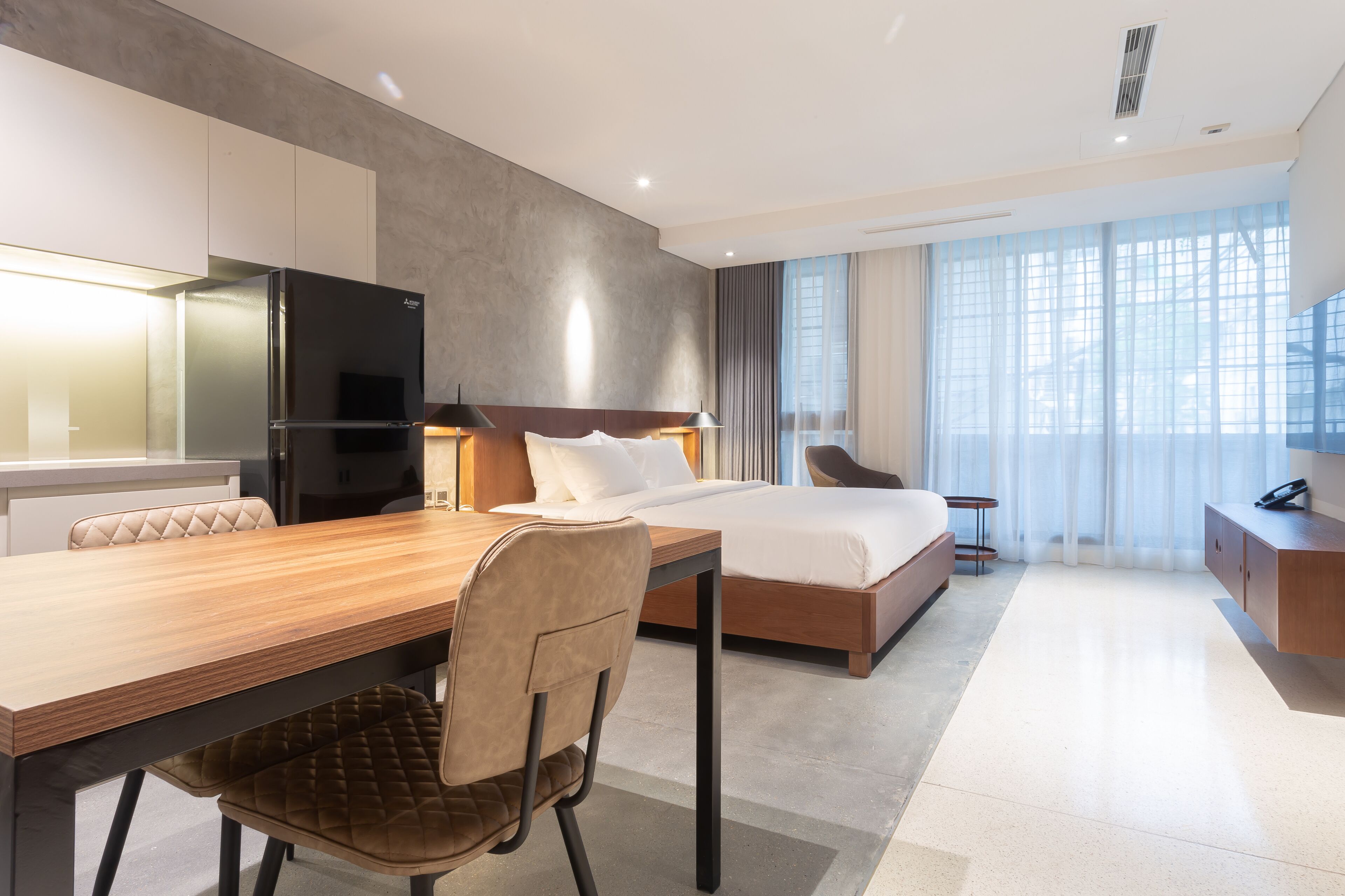 A modern hotel room with a wooden desk, a bed, a chair, and a TV.