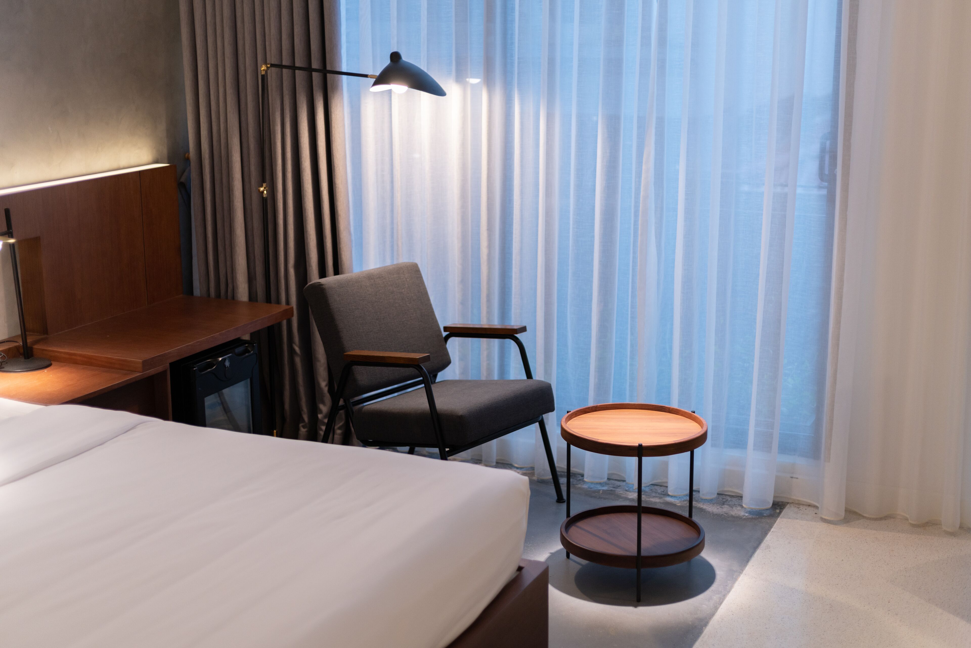 Una camera d'albergo con un letto, una scrivania, una sedia, un tavolino e una lampada.