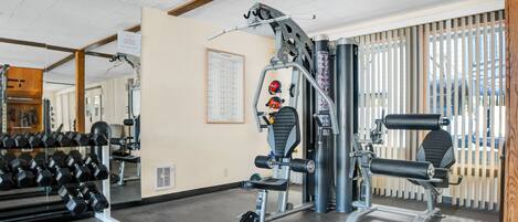 A gym with exercise equipment, a mirror, and a window with blinds.