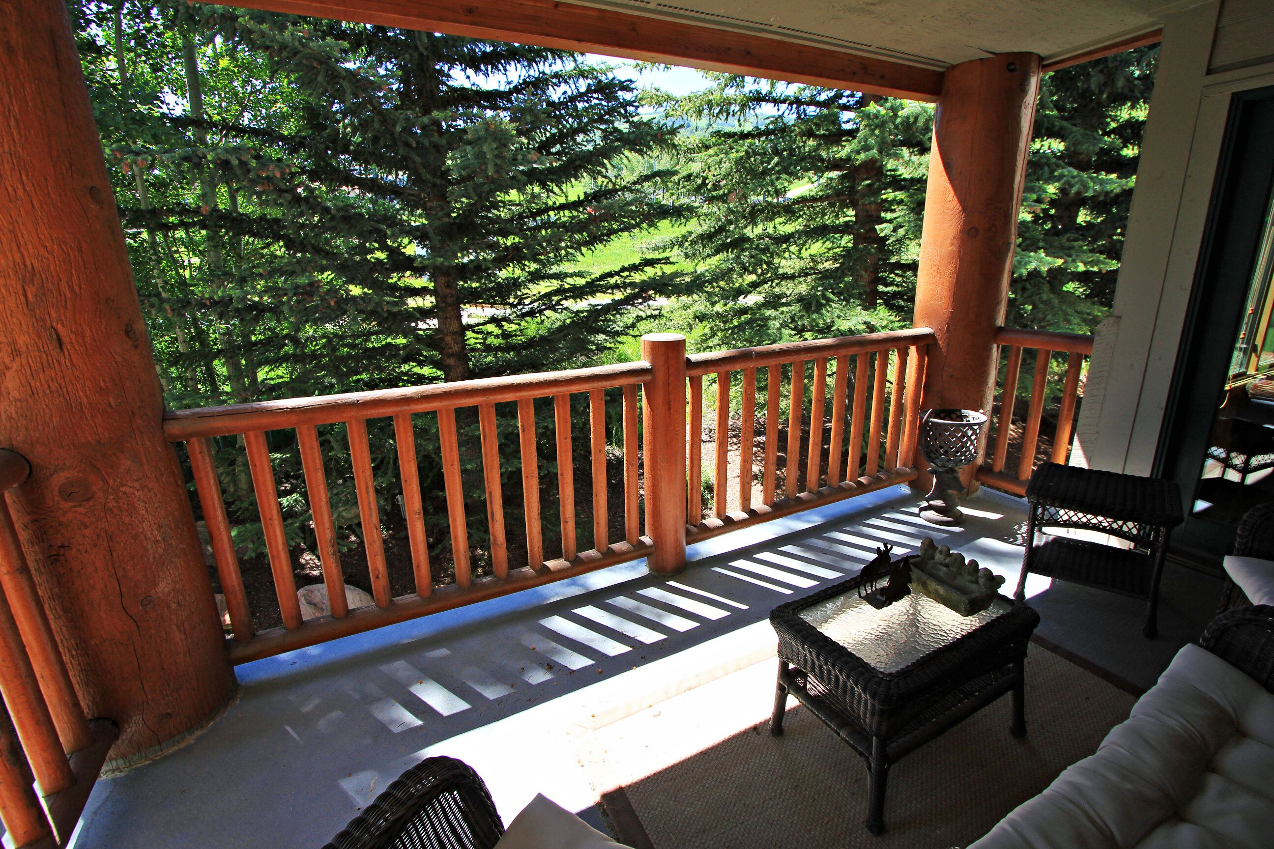 A wooden deck with a railing, a wicker table, and a white sofa.