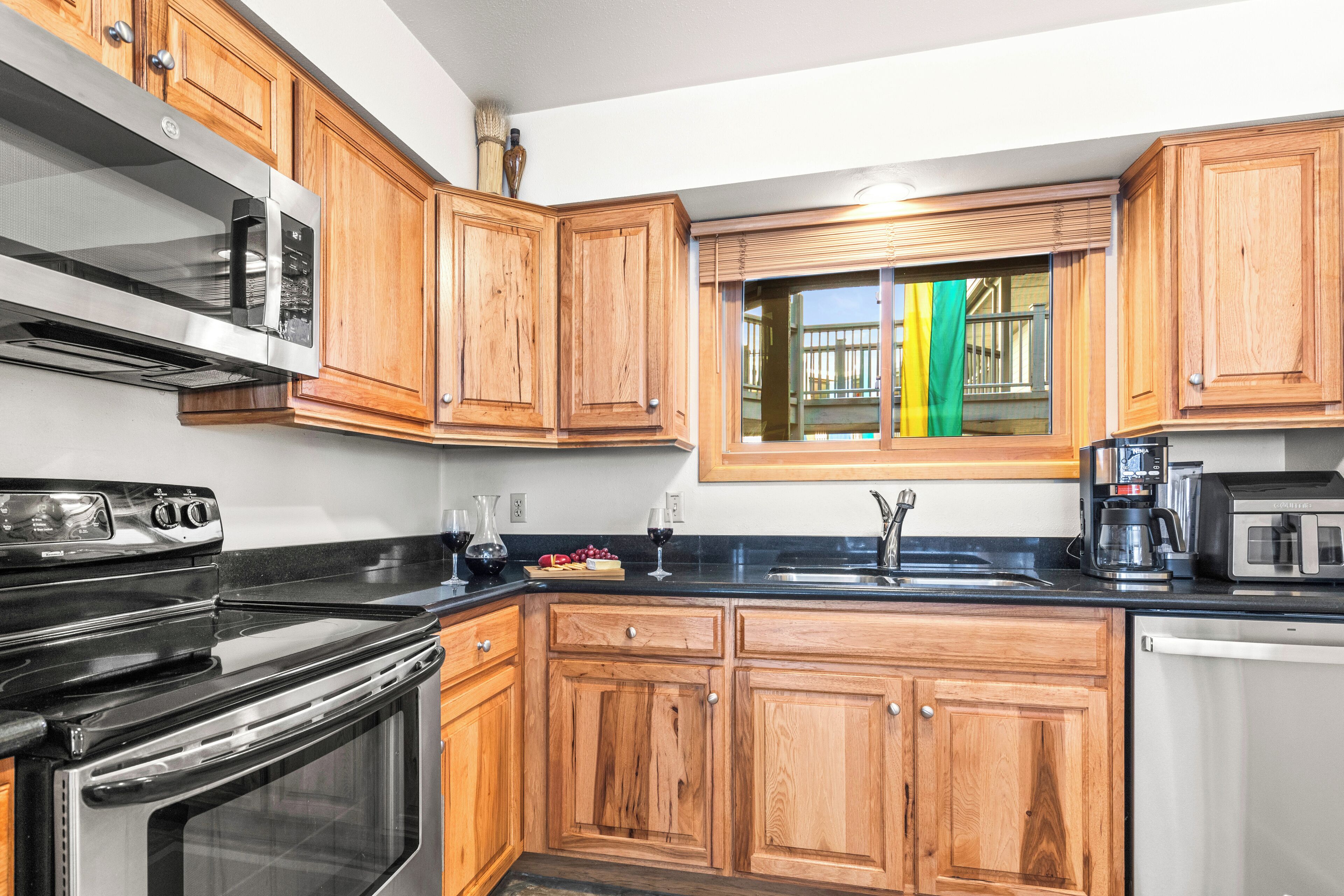 A kitchen with wooden cabinets, a black countertop, a stainless steel microwave, a stove, and a window with colorful curtains.