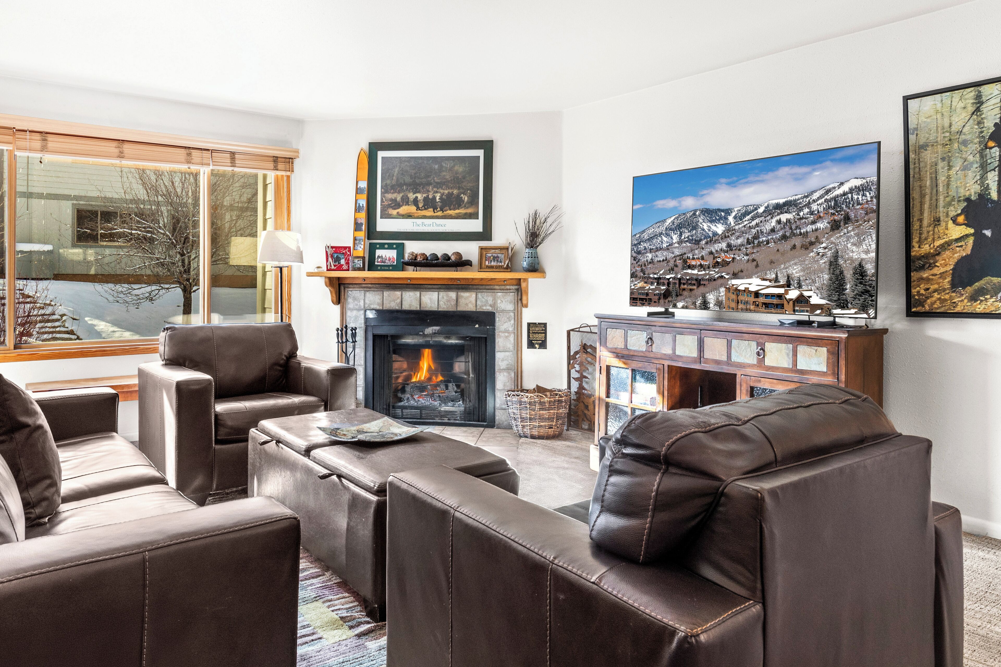 Een moderne woonkamer met leren banken, een open haard en een groot raam met uitzicht op een besneeuwde berg.