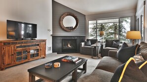 Ein modernes Wohnzimmer mit Flachbildfernseher, Kamin, großem Spiegel und einer gemütlichen Sitzecke mit Sofa und Sesseln.