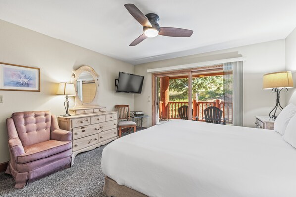 Une chambre avec un grand lit, un ventilateur de plafond, une commode, une chaise, un téléviseur et une vue sur l’extérieur grâce à une porte-fenêtre coulissante.