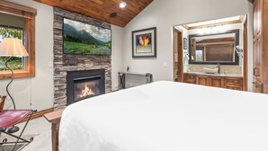 A bedroom with a stone fireplace, a bed, a ceiling fan, and a view of the outdoors. - Managed by Park City Lodging-True Ski-In/Ski-Out to Park City Mountain Resort! (Park City)