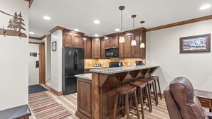 A kitchen with wooden cabinets, a black refrigerator, a microwave, and a bar area with stools. - Managed by Park City Lodging-True Ski-In/Ski-Out to Park City Mountain Resort! (Park City)