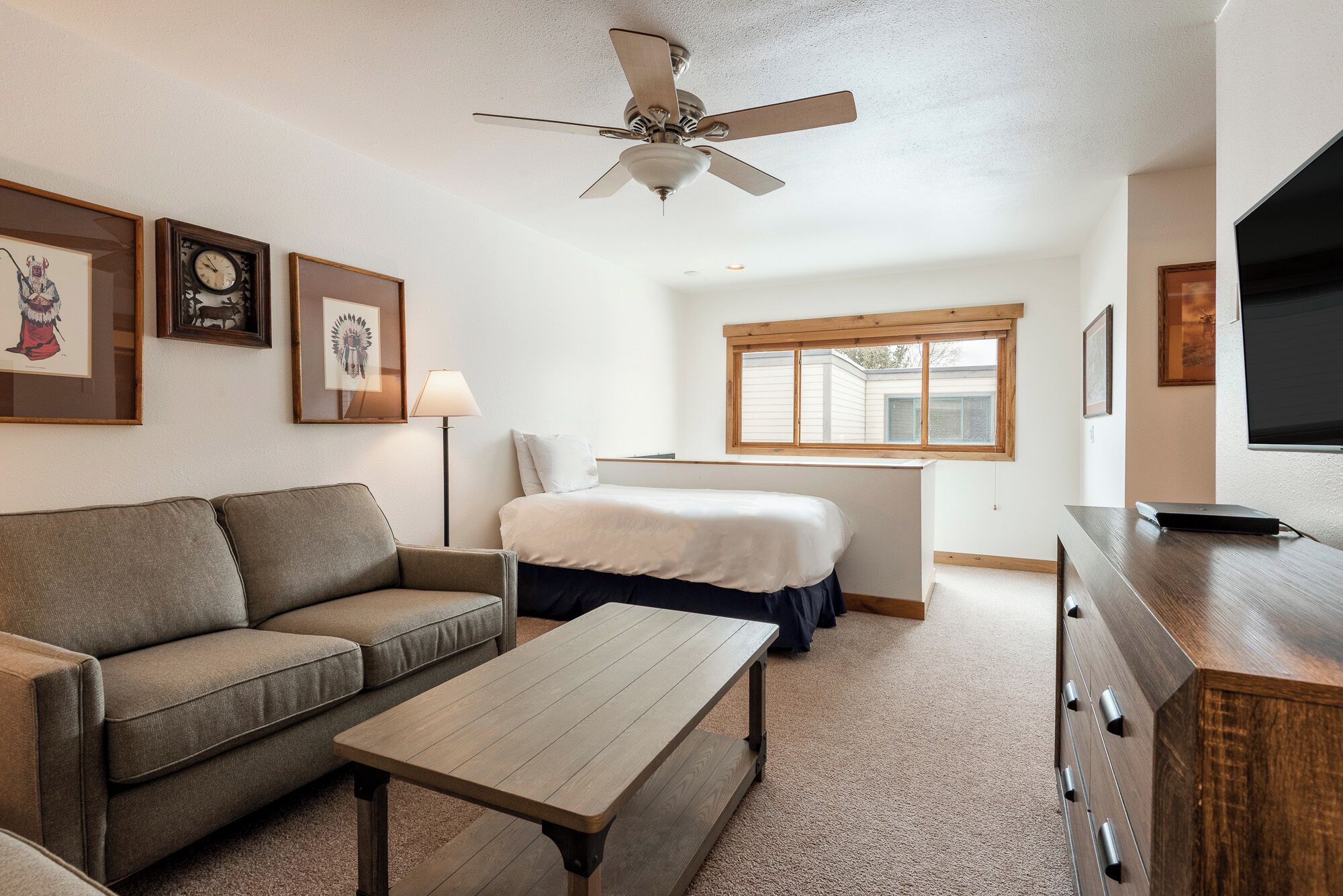 Une pièce de taille modeste comprenant un lit, un canapé, une table basse, un bureau et un ventilateur de plafond.
