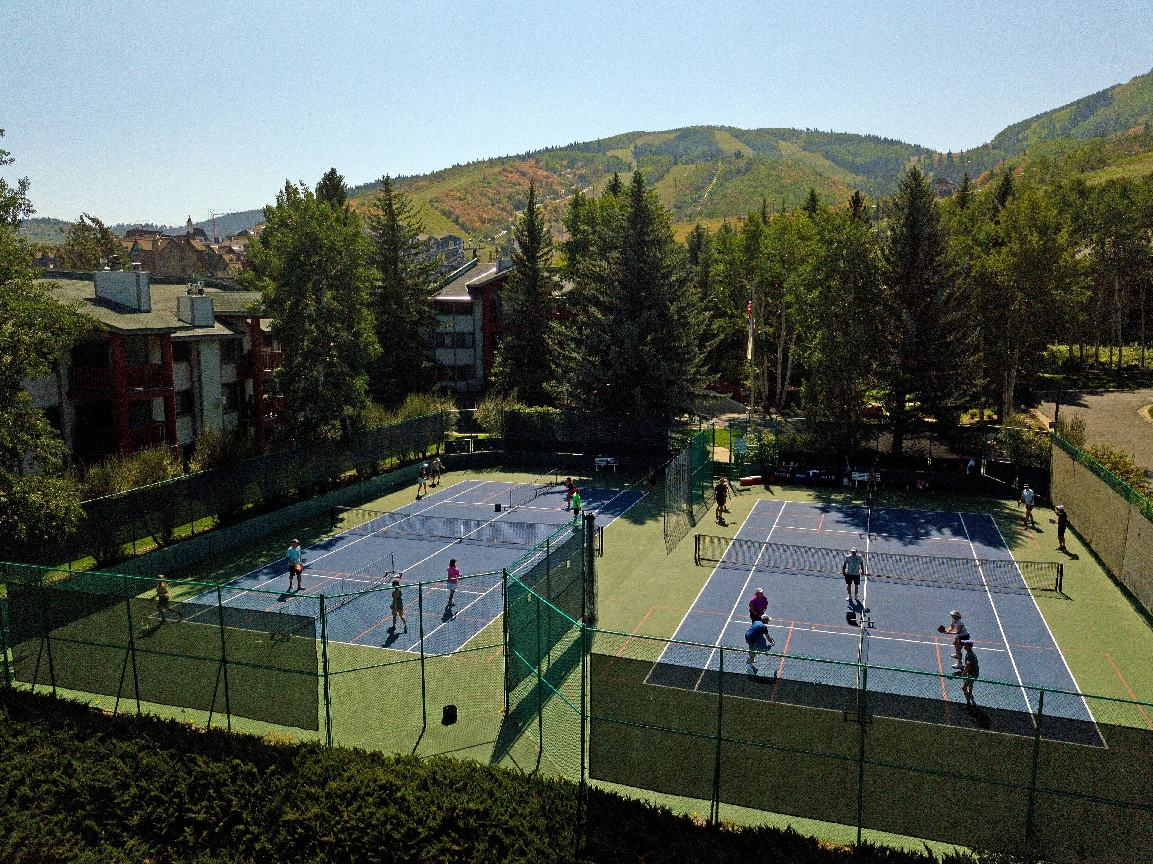 Un court de tennis en plein air, entouré d’arbres et d’immeubles.
