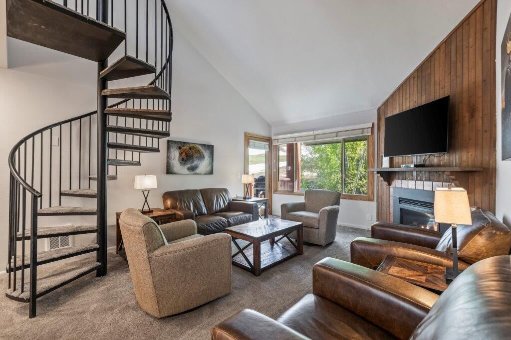 A modern living room with a spiral staircase, leather sofas, a fireplace, and a flat-screen TV.