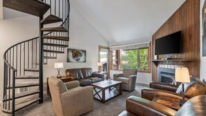 Ein modernes Wohnzimmer mit einer Wendeltreppe, Ledersofas, einem Kamin und einem Flachbildfernseher.
