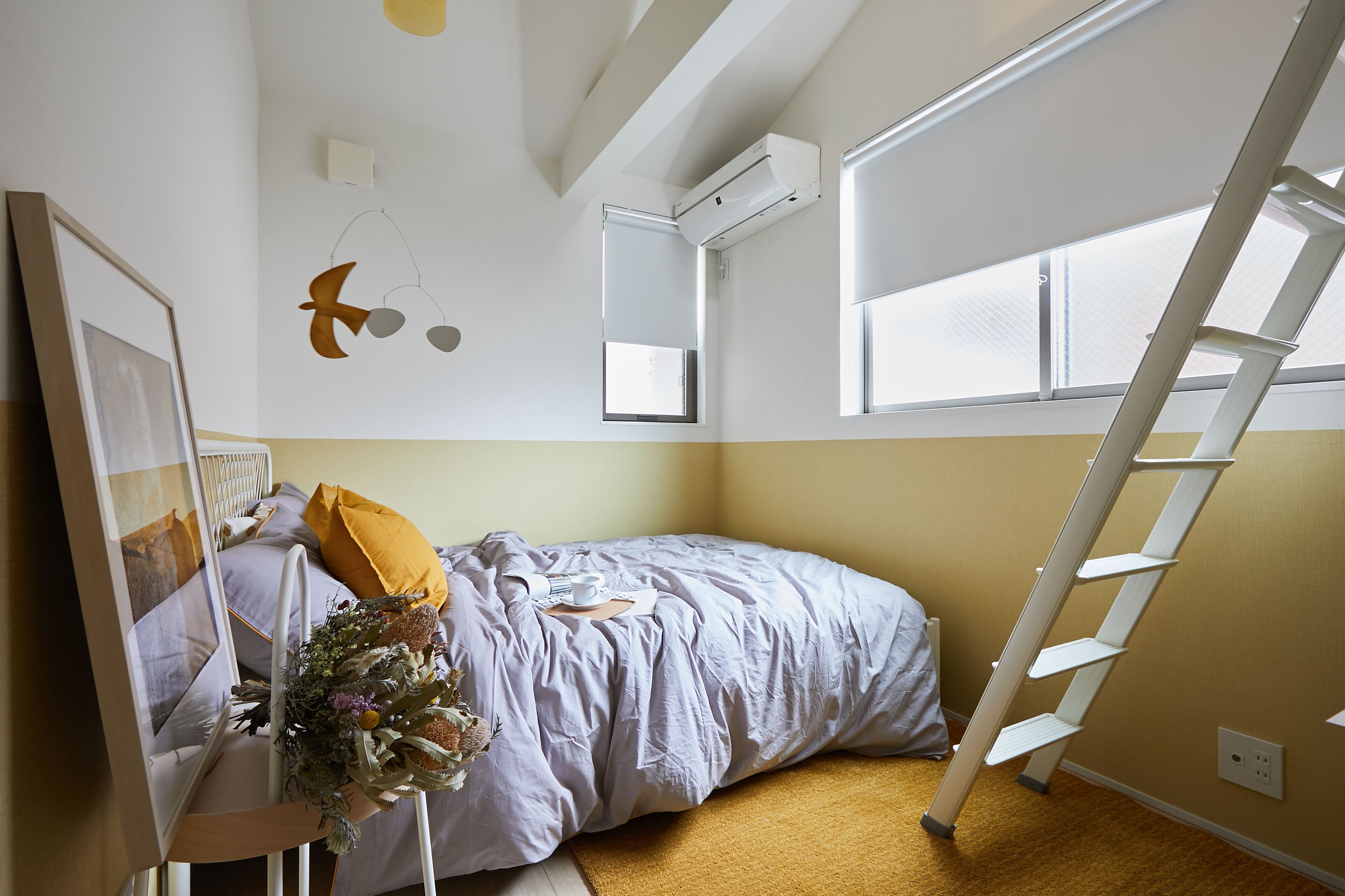 A bedroom with a bed, a ladder, a window, and a wall-mounted air conditioner.