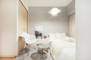 Un dormitorio moderno con una cama, una silla blanca, una mesita redonda pequeña y una lámpara colgante.