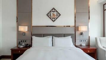 A hotel room with a large bed, two bedside tables, a nightstand, a chair, and a decorative wall piece.