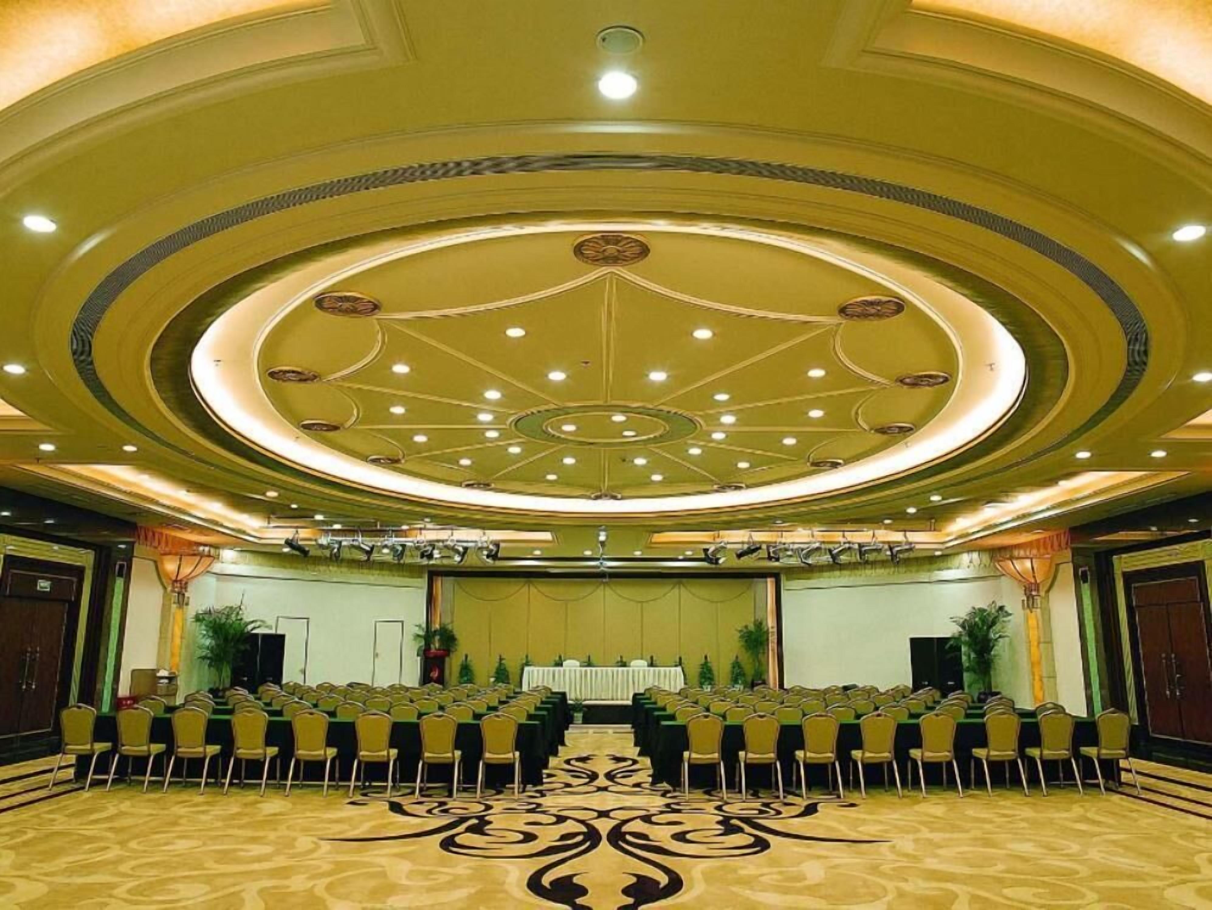 Un salón de conferencias con filas de sillas y un escenario, que cuenta con un techo decorativo y piso alfombrado.