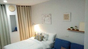 Une chambre à coucher avec un lit, un canapé bleu, une horloge murale et un panneau décoratif encadré.