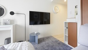 Une chambre d’hôtel moderne avec un téléviseur à écran plat fixé au mur, une petite table ronde avec une tasse, une moquette grise et un canapé blanc.