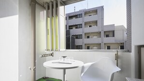 Un petit balcon avec une table et une chaise blanches, une fenêtre donnant sur un immeuble à plusieurs étages et un radiateur.