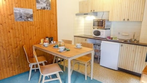 Une petite cuisine avec une table et des chaises en bois, un four à micro-ondes, un évier et un réfrigérateur.