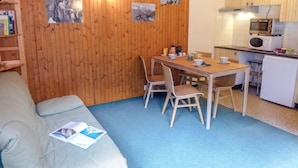 Une pièce de taille modeste avec un mur en bois, une table à manger avec des chaises, un coin cuisine et un canapé avec un magazine.
