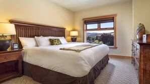 A hotel room with a large bed, two bedside tables with lamps, a dresser, and a window with a view of the outdoors. - Lake Chelan - Lake House (Chelan)