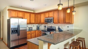 A kitchen with wooden cabinets, stainless steel appliances, granite countertops, and bar stools. - Lake Chelan - Lake House (Chelan)
