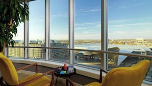 A room with large windows, two yellow chairs, a small table with a drink and a puzzle, and a plant. - Rotterdam Marriott Hotel (Rotterdam)