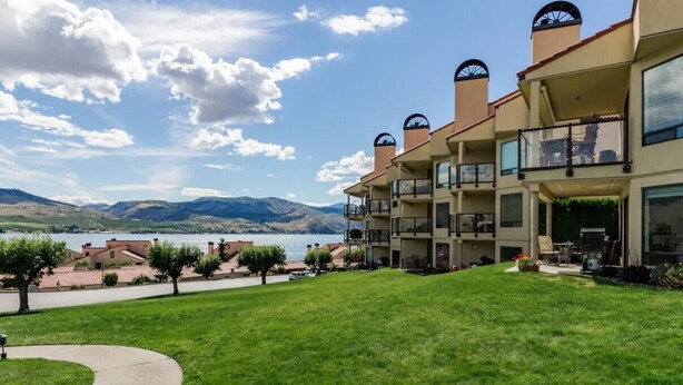 Un hotel de varios pisos con balcones que dan a un lago y montañas.