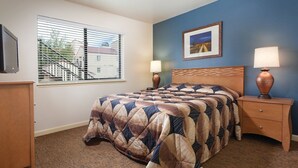 Un dormitorio con cama, mesita de noche, lámpara, cómoda, ventana con persianas y un cuadro en la pared.