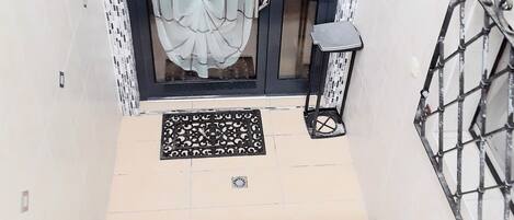 A staircase leading to a door with a patterned mat, a metal gate, and a tiled wall with a mosaic border.