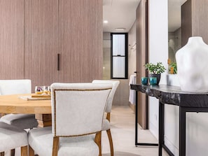 A modern dining area with a wooden table, white upholstered chairs, and a black marble countertop with a vase and plant.