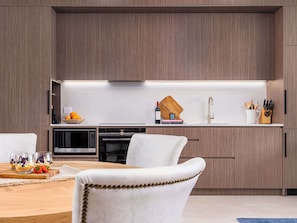 A modern kitchen with built-in appliances, a wooden countertop, and a dining area with a white chair.