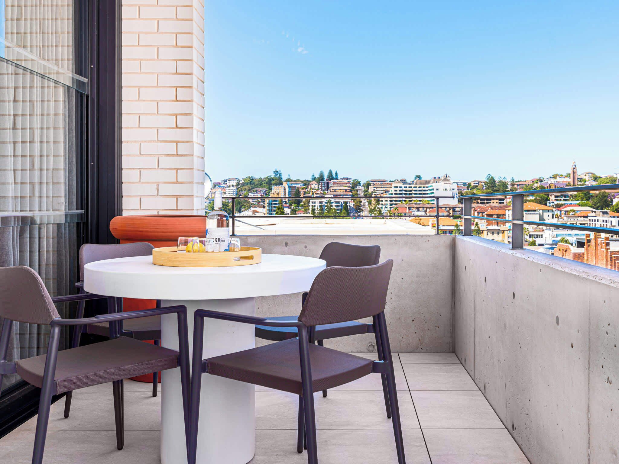 A balcony with a round table and chairs, a bottle, and a tray with lemons.