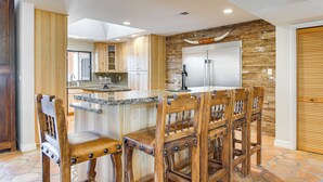 Une cuisine moderne avec des meubles en bois, un îlot central doté de tabourets de bar et un grand réfrigérateur.