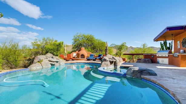 Une piscine avec un jacuzzi, des chaises longues et un espace barbecue.