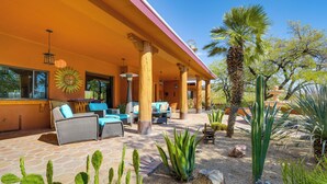 Une terrasse extérieure couverte, aménagée avec des meubles en osier, un jardin de cactus et un palmier.