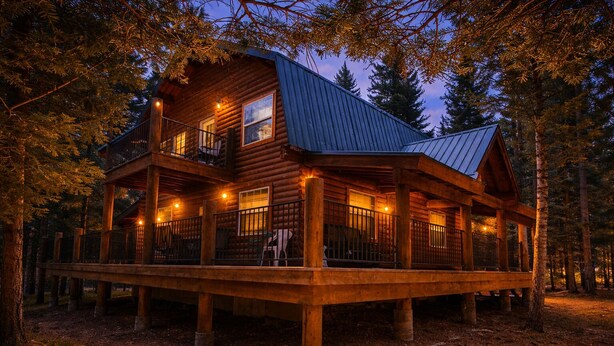 A log cabin with a balcony, a covered deck, and a metal roof, surrounded by trees.