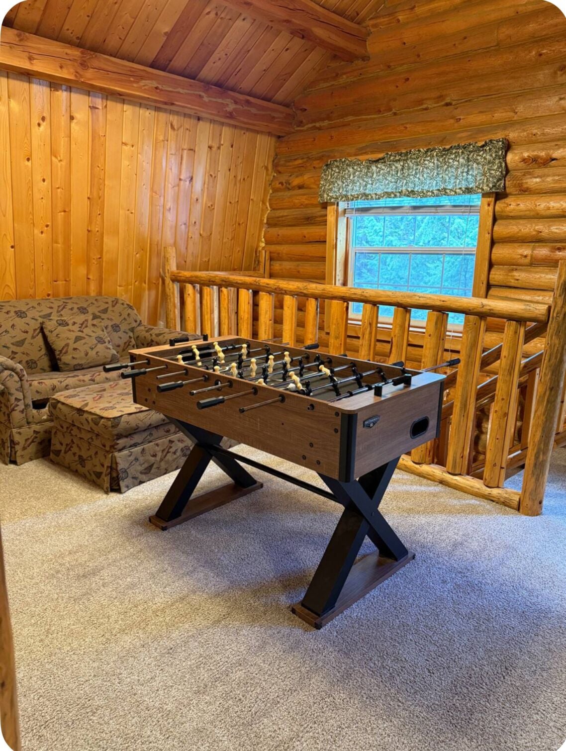 A cozy room with a wooden interior, a foosball table, a sofa, and a window with a view.